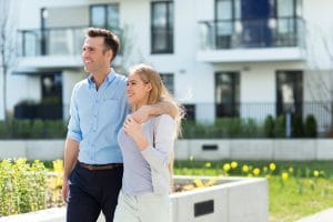Smiling Sydney homeowners walking together outdoors in front of a modern apartment building, symbolising property ownership.